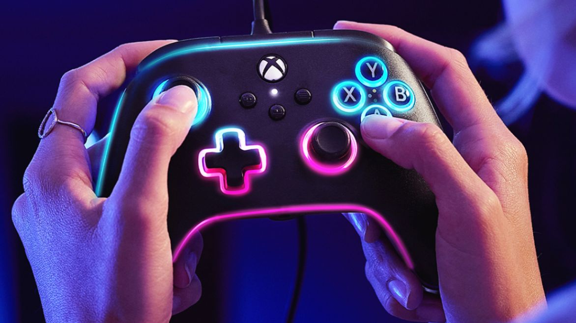 Someone holding a black wired Xbox controller with light blue and pink RGB lighting around all the trim.