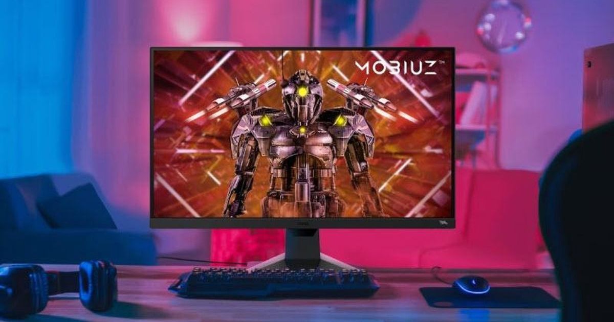 A black monitor with a robot on the display sat on a desk surrounded by pink and blue light.