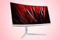 A silver curved gaming monitor with a dark red pattern on the display in front of a gradient red and white background.
