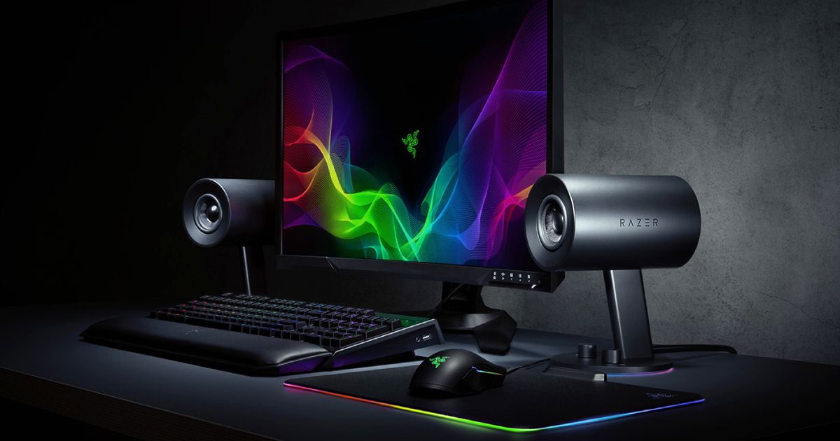 A black monitor with a multicolour pattern on the display next to a set of black speakers and an RGB keyboard.