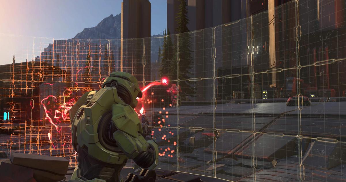 Halo Infinite's Master Chief shoots enemies from behind a shield.
