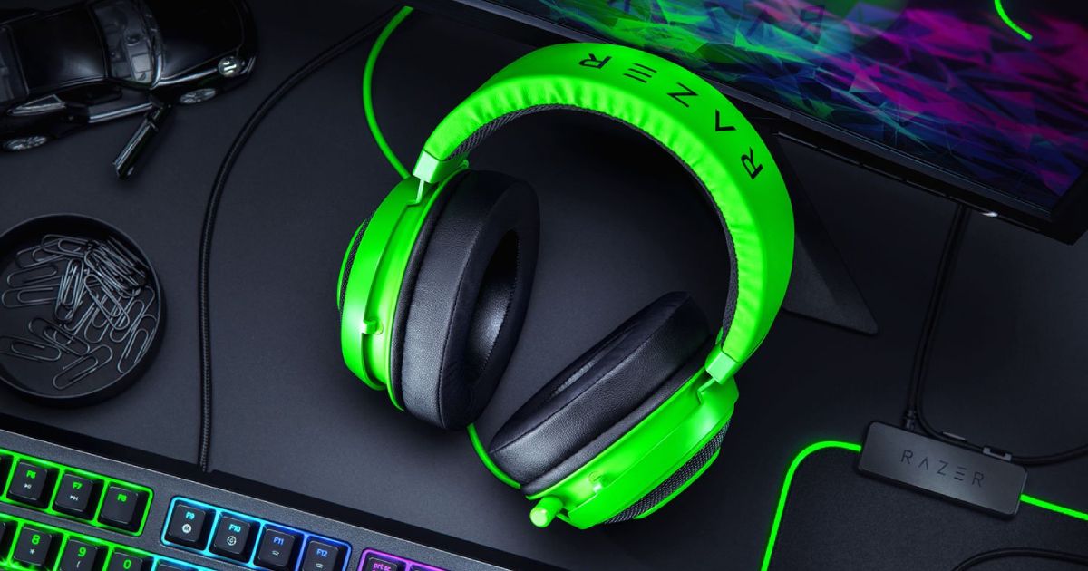 A green over-ear headset with black earcups sat on a desk next to Razer gaming accessories.