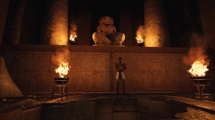 The Forgotten City. Khabash is standing in front of a large hole in the ground in the catacombs. There is an Egyptian statue behind and slightly above him. There are four flame-lit torches around him