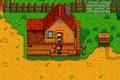 Stardew Valley. Standard Farm in Spring Year 1. The player, Marnie and a dog are standing on the wooden decking of the house. The ground around the farm is bare.