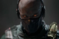 A bald man with glowing orange eyes and a black mask covering his mouth and nose