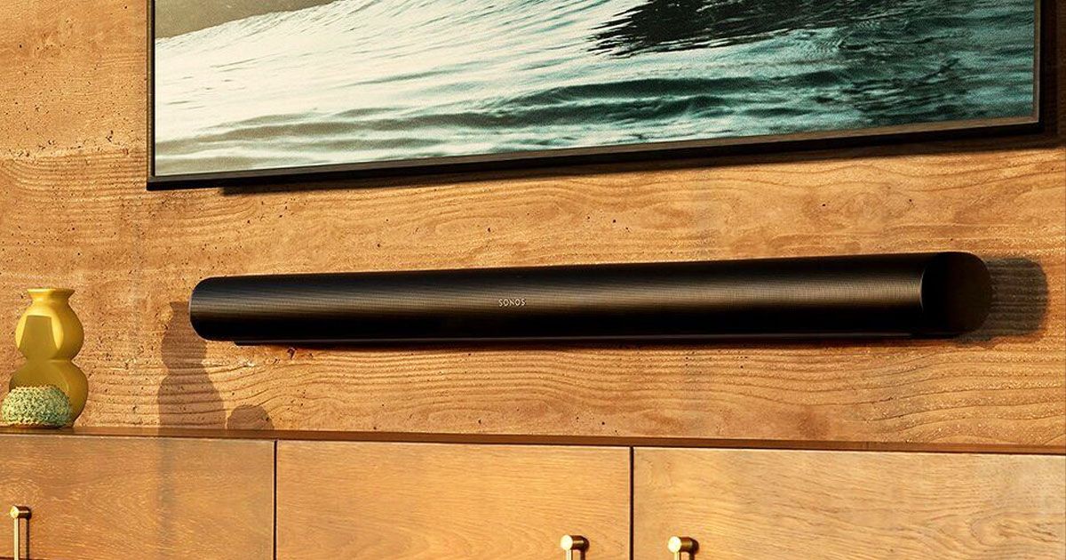 A thin black soundbar mounted to a brown wooden wall below a flatscreen TV.