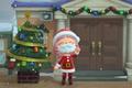 An Animal Crossing: New Horizons player stands outside of the Resident Services building in their Santa outfit, besides a Festive Tree crafted using a festive DIY recipe and ornaments.
