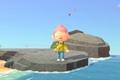 Animal Crossing New Horizons, the player is stood on a rock near the edge of the ocean and they are holding their slingshot. Their eyes are closed.