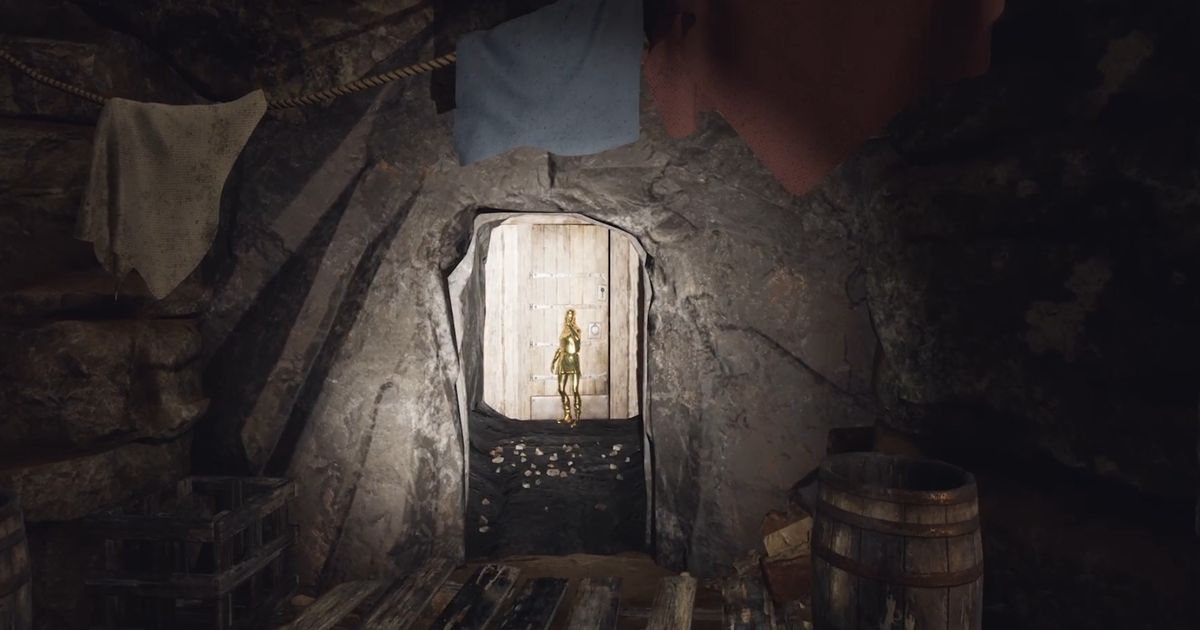 The Forgotten City. A golden statue is blocking a doorway. There are pieces of cloth hanging on the stone wall above the doorway. A torch is lighting up the small doorway and statue.
