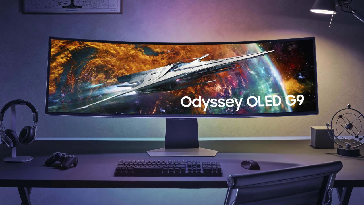 An ultrawide Samsung monitor sat at a desk in a dark room, complete with a headset, controller, keyboard, and mouse around .it.