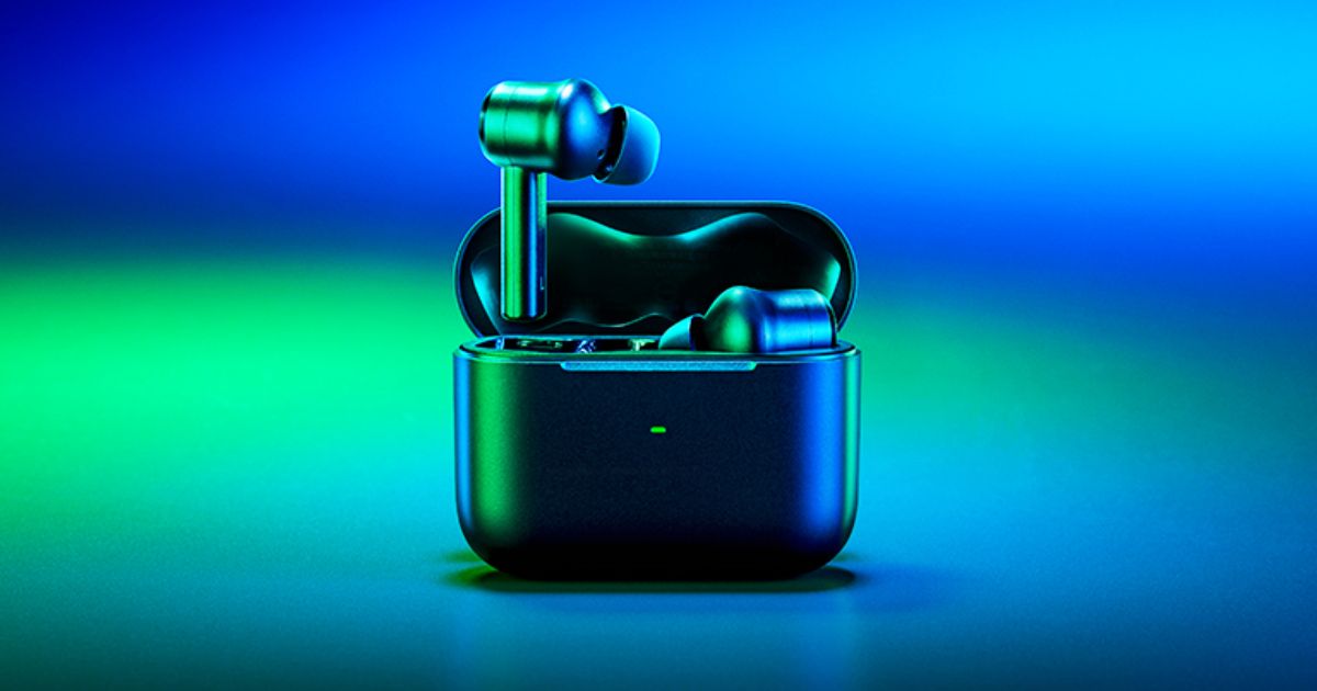 A pair of black wireless earbuds in their charging case bathed in blue and green light.