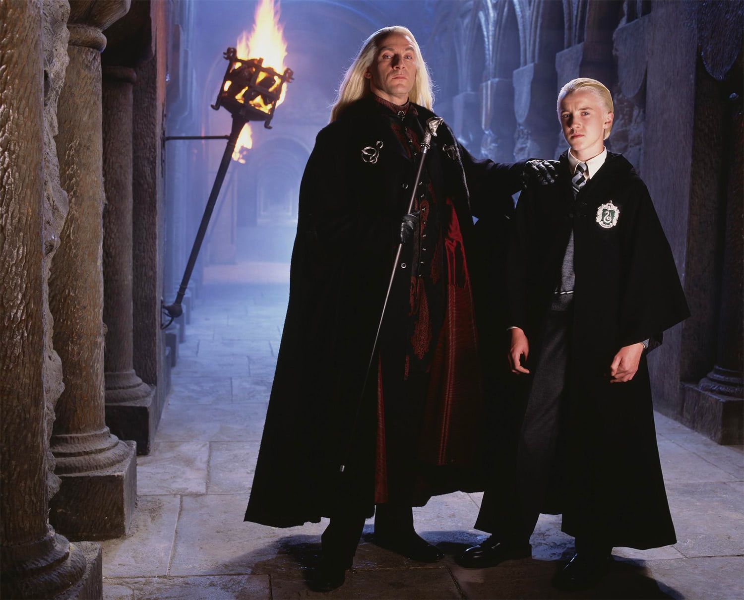 Lucius (left) and Draco Malfoy (right) are in a Hogwarts hallway.