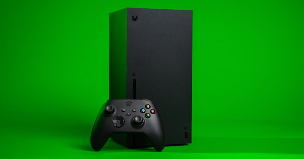 A black Xbox Series X with a controller leaning against it in front of a green background.