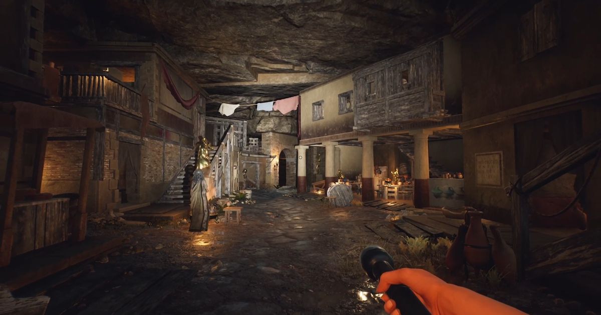 The Forgotten City, The Slums. The image shows the slums being lit by a torch beind held by the player. Livia is standing on the right with her back to the player. The slums are dimly lit with some cloth hanging from the ceiling at the back.