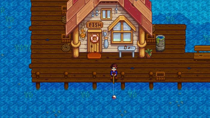 Stardew Valley. The player is standing on the dock in front of the Fish Shop. They are standing on the edge of the wooden dock and fishing over the edge. 