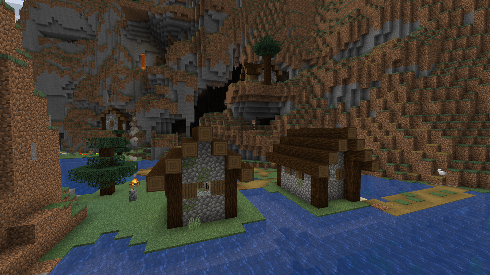 A Minecraft village at the bottom of a ravine, with the opening to a large cave behind it.