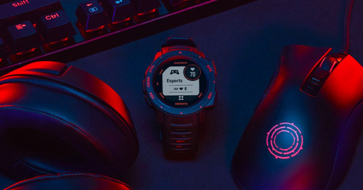 A black smartwatch next to a mouse, headset, and keyboard, all bathed in red light.