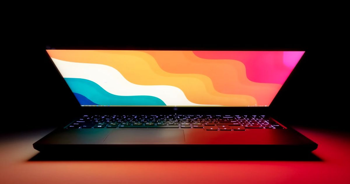 A half-closed laptop with backlit keys and a pink, orange, yellow, and blue wavy pattern on the display.