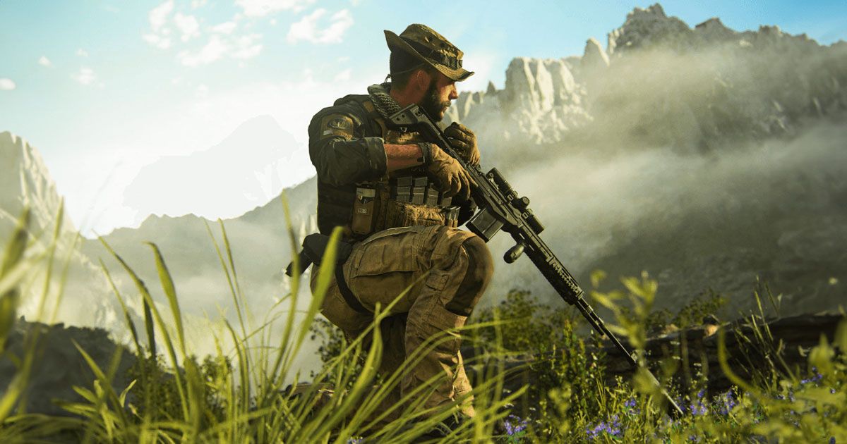 A solider in dark green and biege combat clothing holding a black rifle while crouched in long grass.