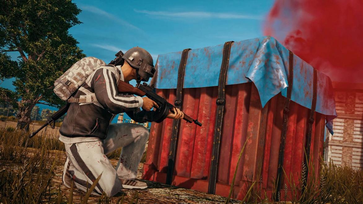 PUBG player crouching next to red and blue care package