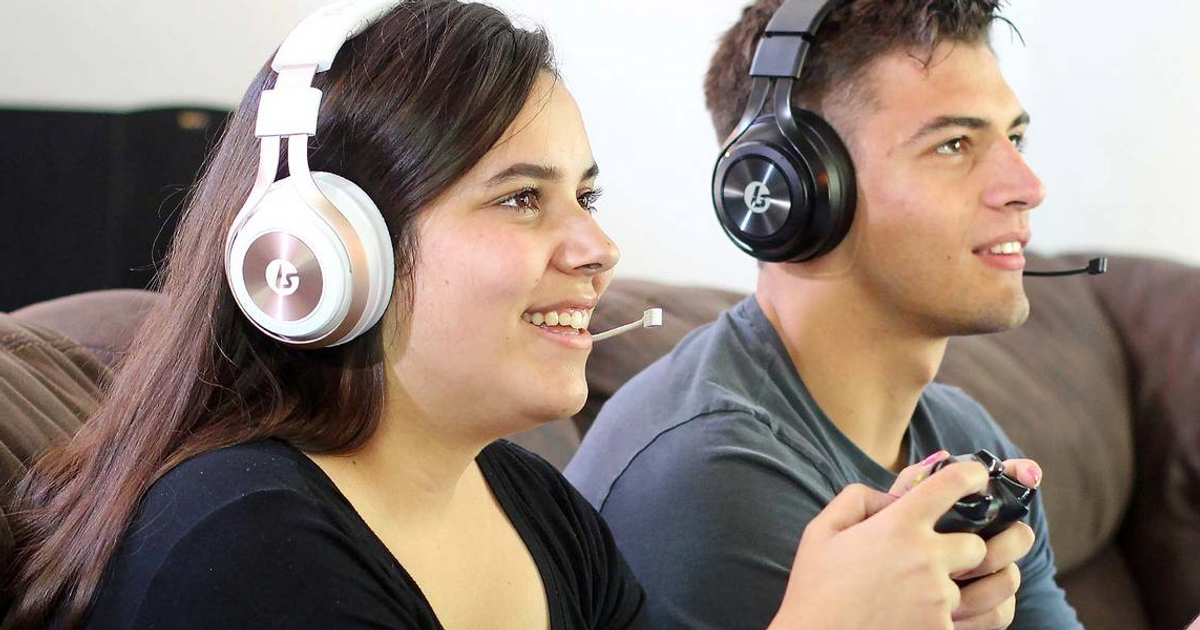 LucidSound LS35X Wireless Gaming Headset - Promotional image showing two adults playing games, woman is wearing the Rose Gold/White LS35X headset. Man is wearing a Black LS35X headset. 