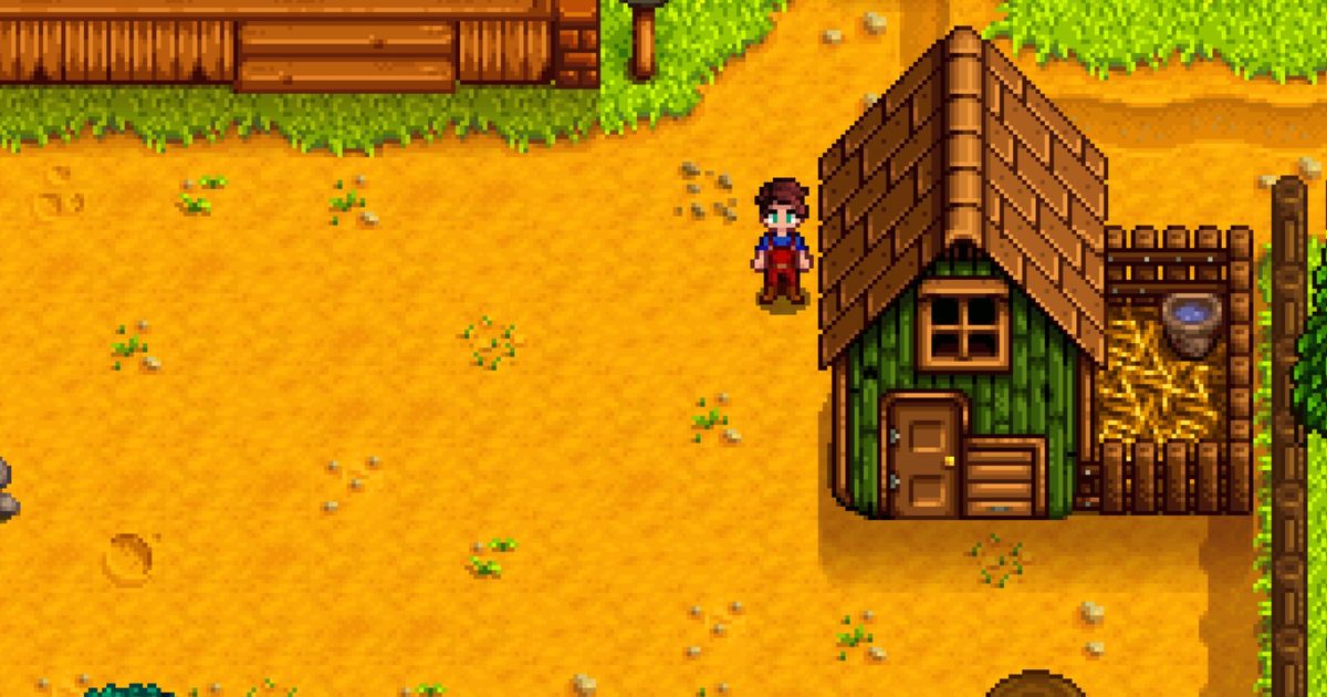 Stardew Valley. The player is stood to the left of their basic coop. The coop is on the right. It's green with a brown door and brown roof. There is a small brown fence holding hay and a bucket of water on the right of the coop.