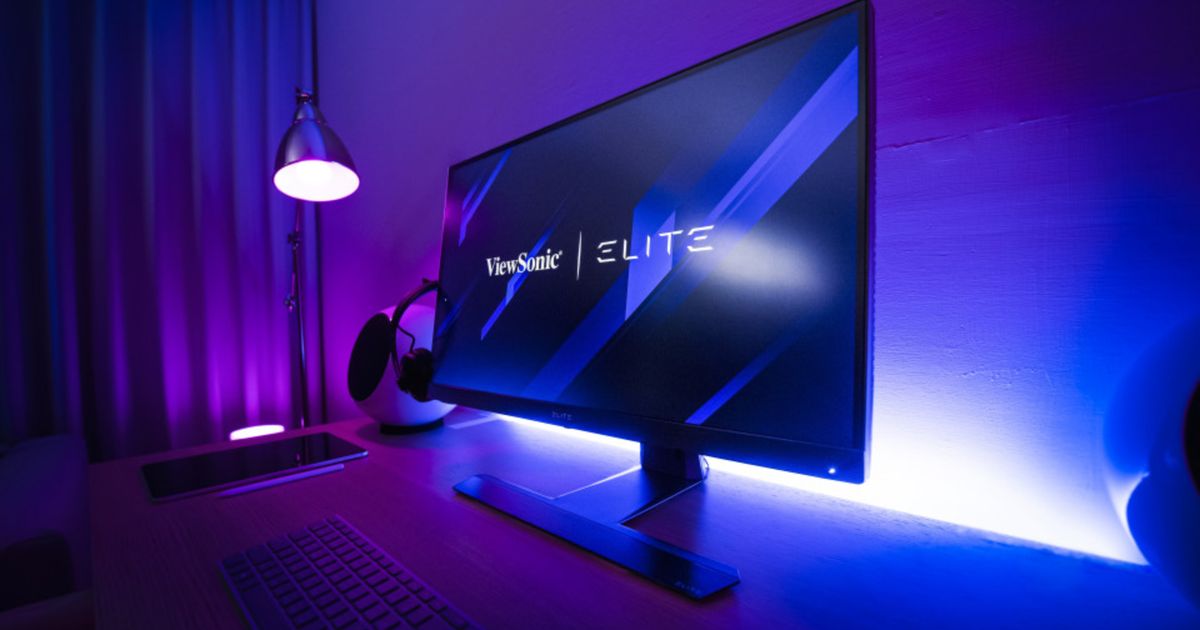 A black monitor sat at a desk with blue and purple lighting behind it.