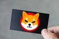 Thumb holding a black gift card with the Shiba Inu Logo.