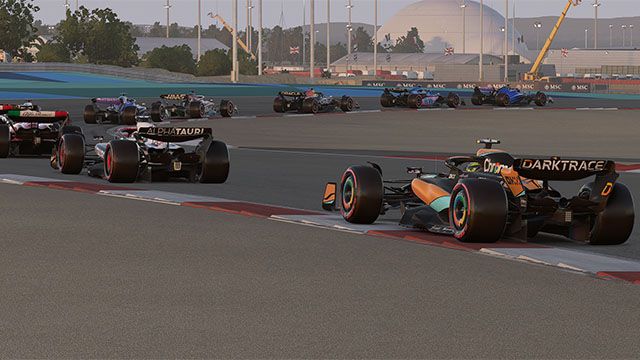 Screenshot of F1 23 cars driving around Bahrain circuit at dusk