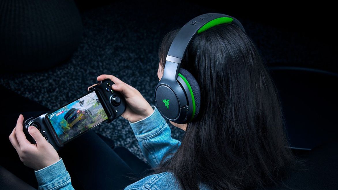 Someone with a black and green over-ear headset on playing a racing game on their phone using a controller.