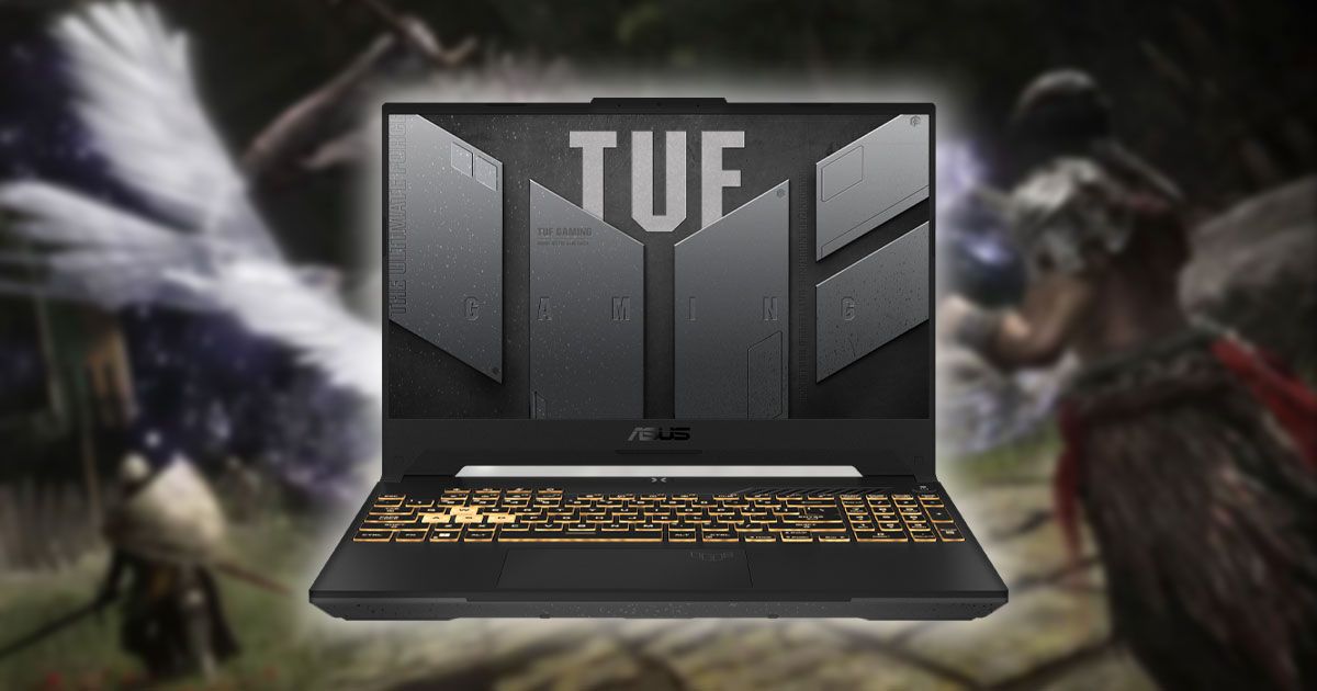 A black laptop with grey TUF branding on the display and yellow lighting behind the keys. The laptop is in front of a blurry image from Elden Ring.