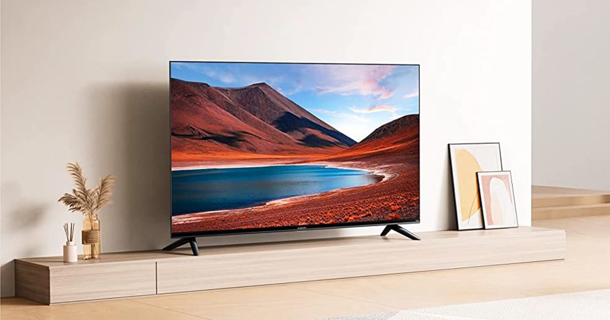 Image of a flat Xiaomi TV on a wooden stand with mountains and a lake on the display.