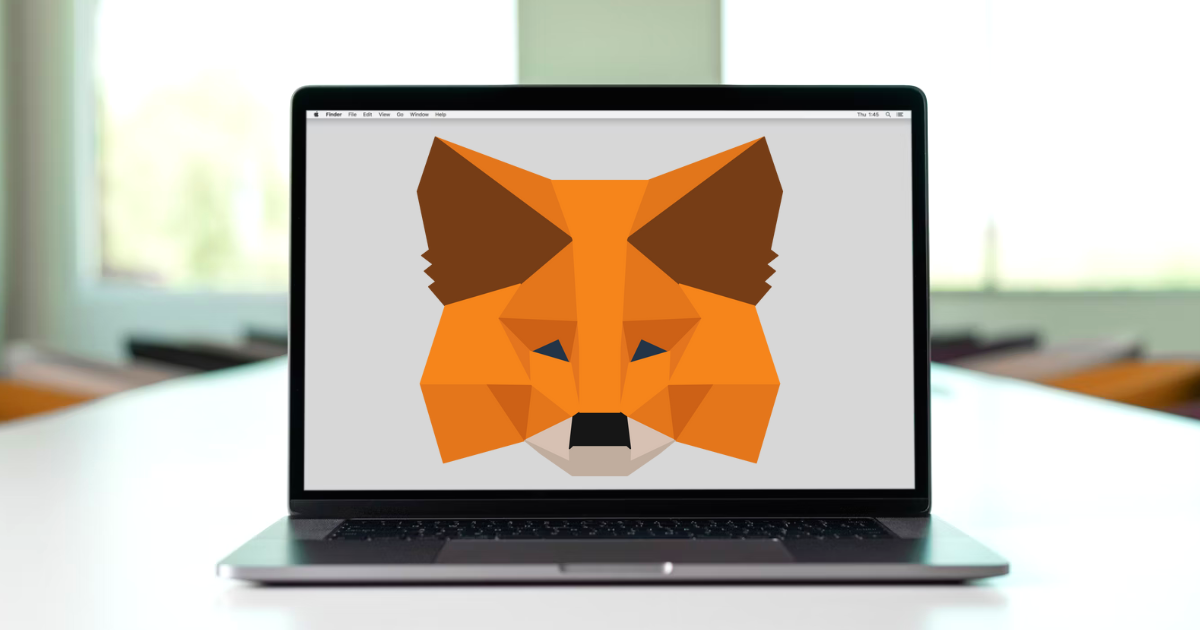 MetaMask logo on a MacBook laptop screen, sat on a table in front of a window