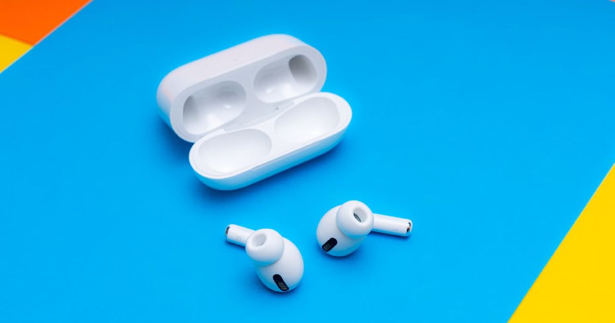 A pair of white AirPods next to a open charging case on a blue surface.