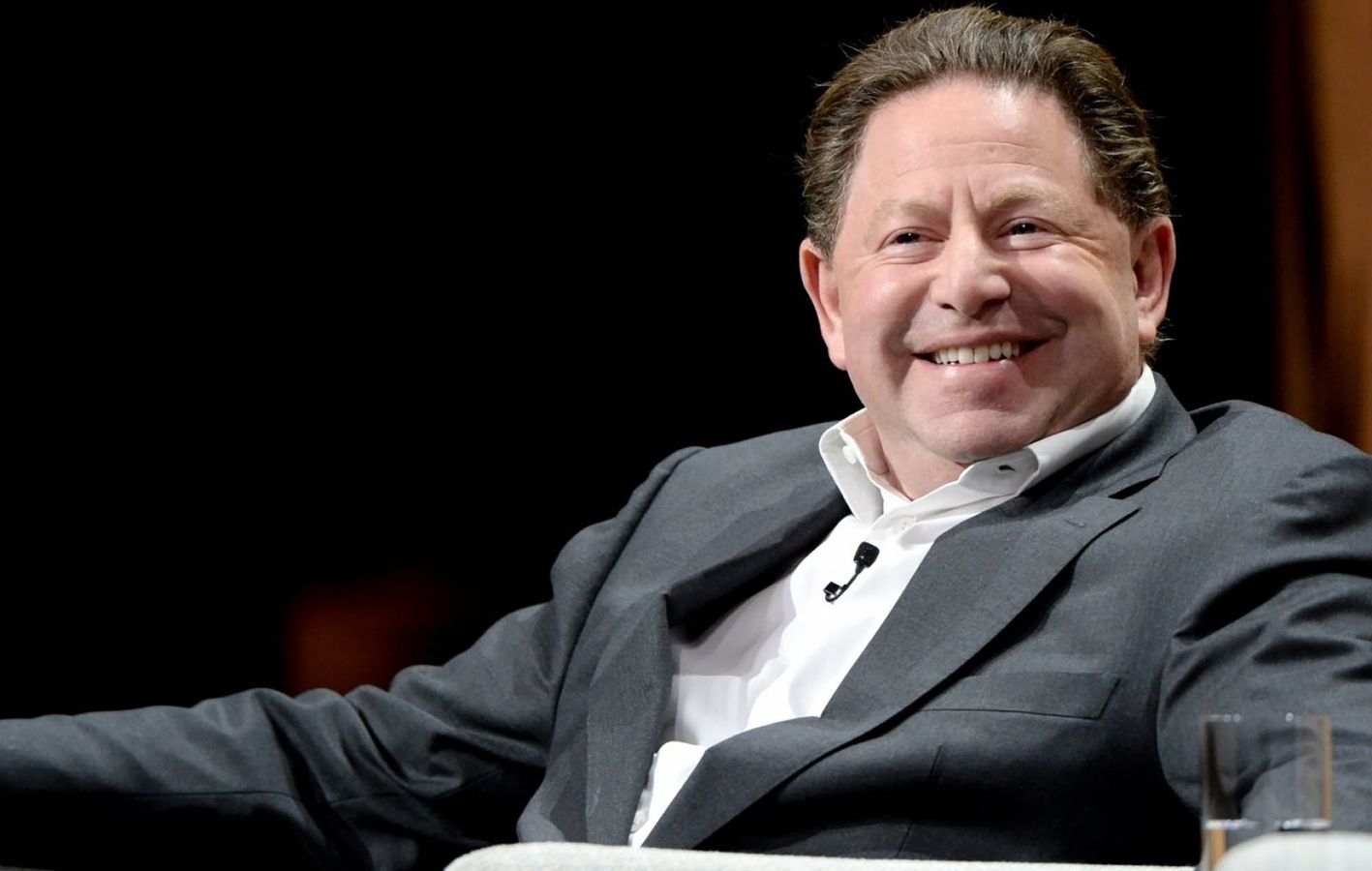 Bobby Kotick, Activision Blizzard's CEO, wearing a grey suit and sat down. Glass of water next to him on right side of image.