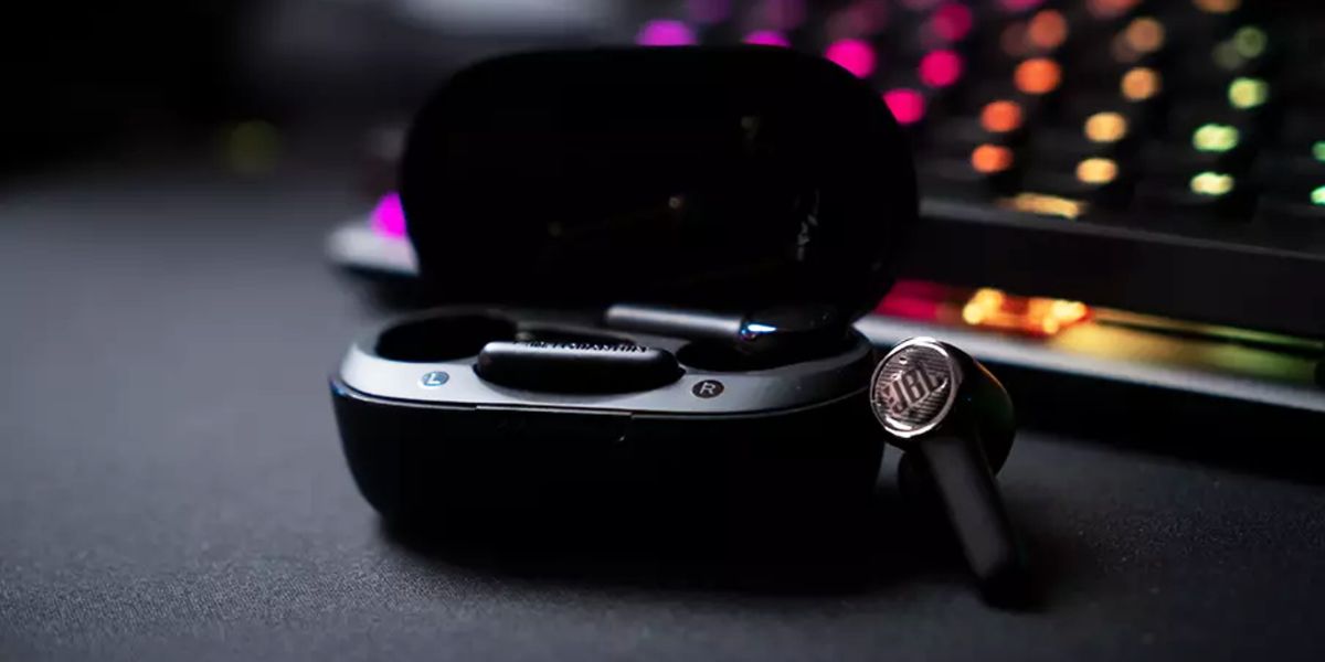 Image of a black, rounded charging case with a JBL wireless earbud leaning against it.